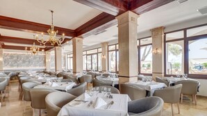 Un restaurante con varias mesas y sillas, ventanas amplias y un candelabro.