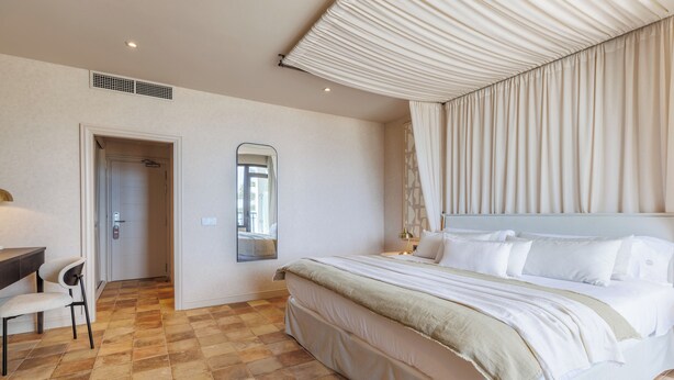 Habitación de hotel con una cama grande, un escritorio con silla, un espejo y una puerta que da al baño.