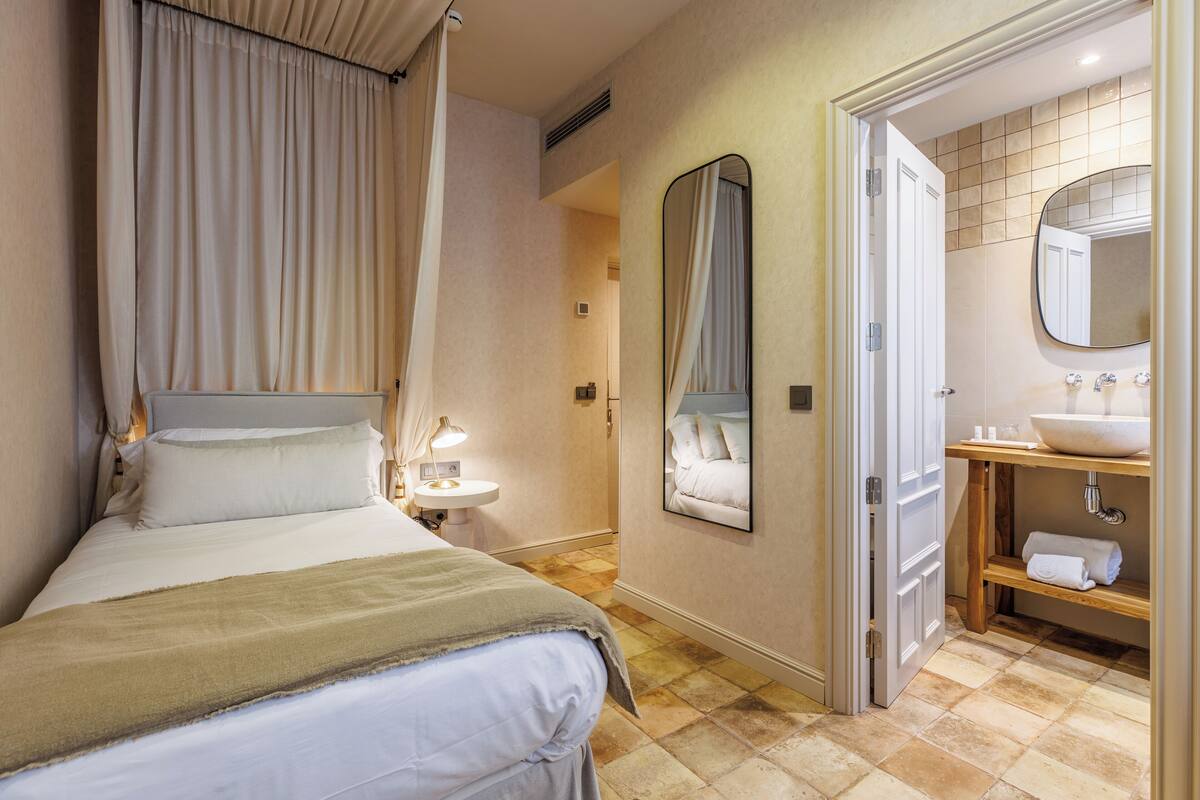 Quarto de hotel com cama, abajur e banheiro com pia e espelho.