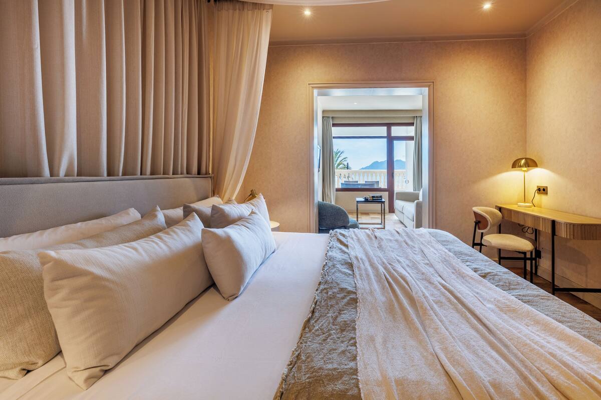 Quarto de hotel com uma cama grande, uma escrivaninha e uma cadeira. Há uma janela com vista para o exterior.