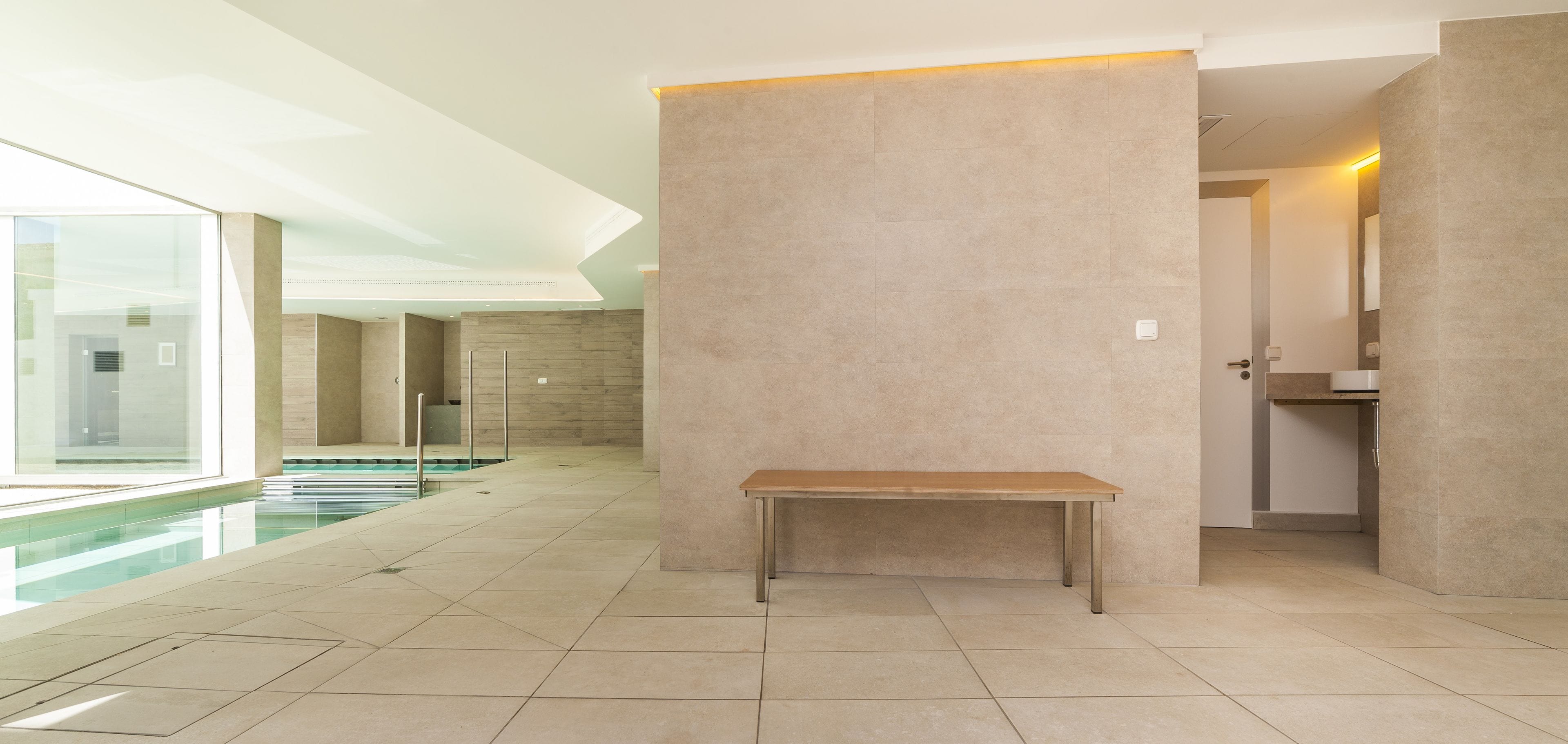 A modern indoor pool area with a bench, glass walls, and a tiled floor.