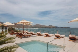 A poolside area with lounge chairs and umbrellas, overlooking a body of water and distant hills. - Hoposa Uyal (Pollenca)