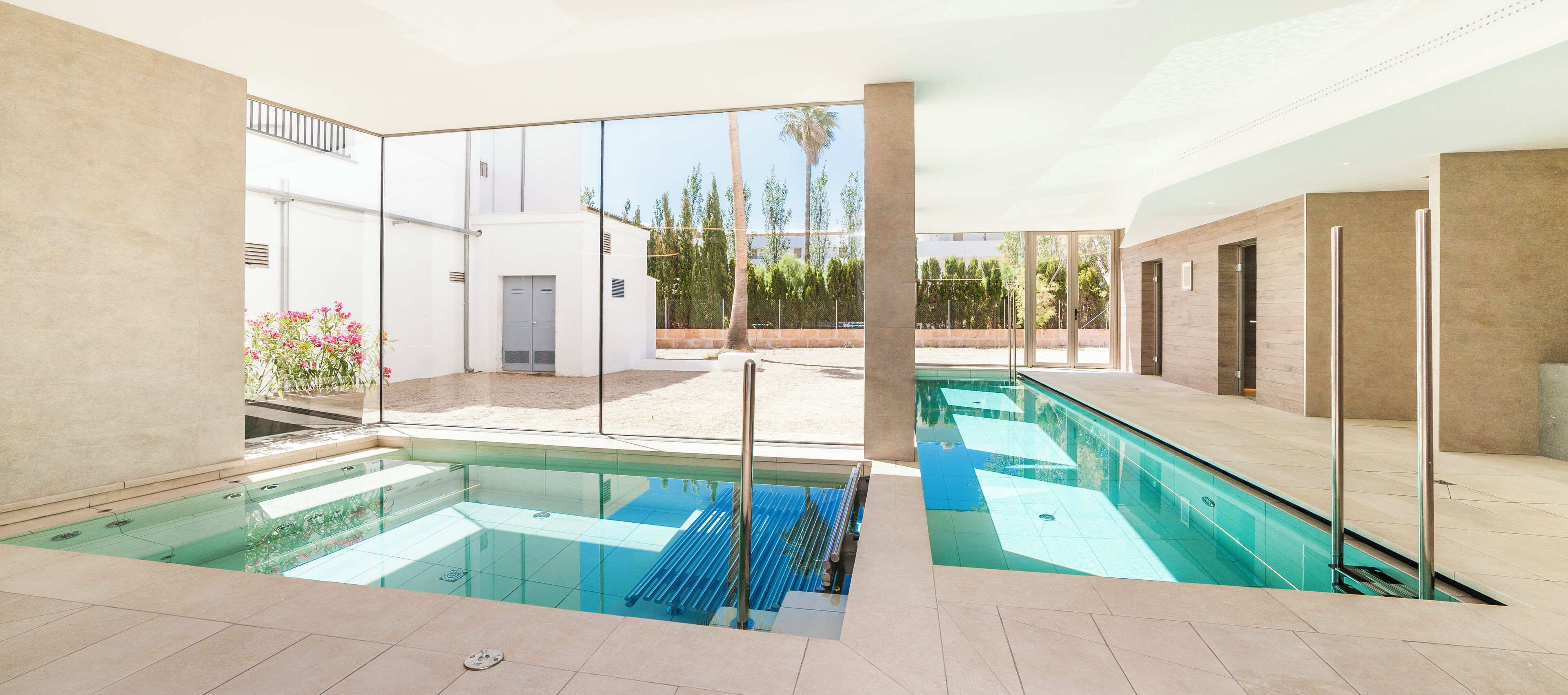 Ein moderner, überdachter Schwimmbereich mit Glaswänden, freiem Blick ins Freie und einem klaren, minimalistischen Design.