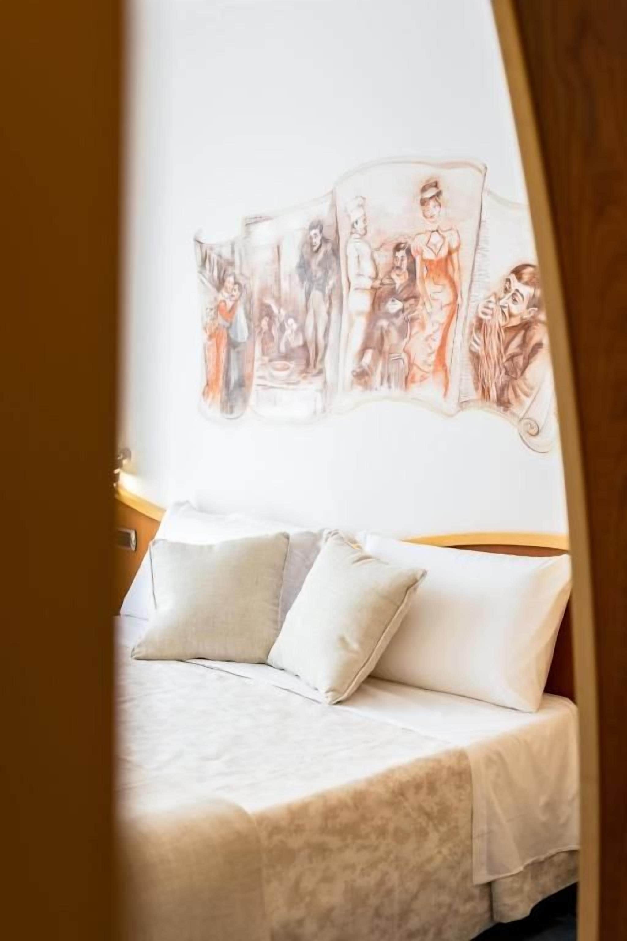 A bed with a white bedspread and pillows, a wall with a series of sketches, and a wooden headboard.