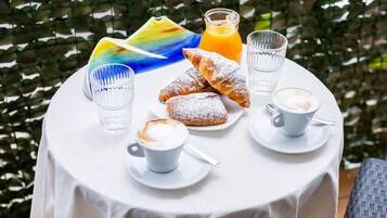 A round table with a white tablecloth, a plate of pastries, two glasses of orange juice, and two cups of coffee.