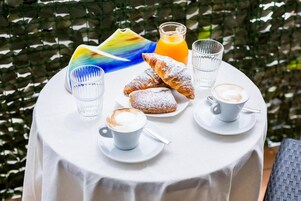 Una mesa redonda cubierta con un mantel blanco, un plato de pasteles, dos vasos de jugo de naranja y dos tazas de café.