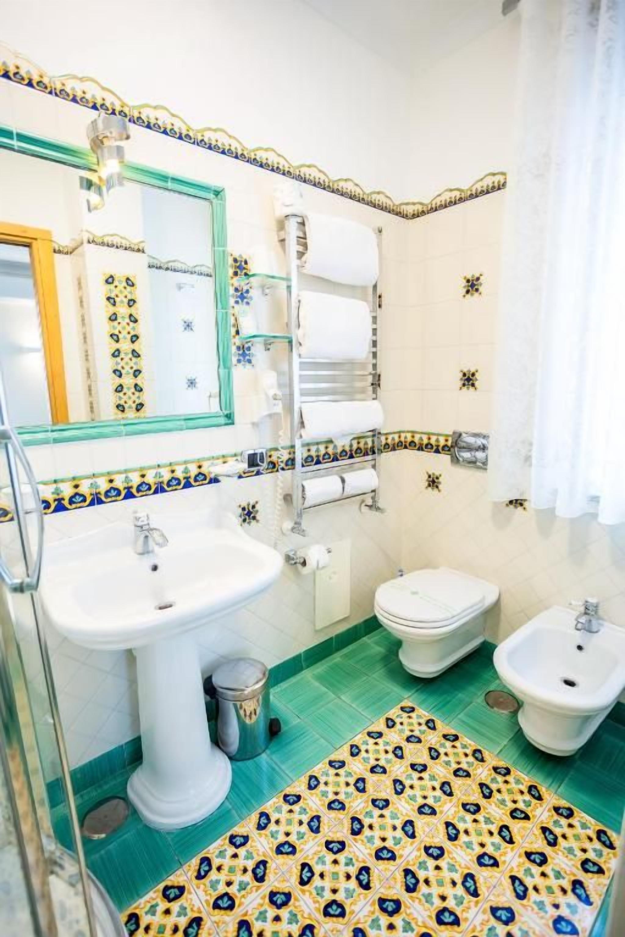 A bathroom with a sink, toilet, bidet, and a patterned floor.