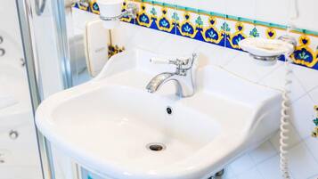 Un lavabo de salle de bain avec un receveur en porcelaine blanche, un robinet chromé et un téléphone fixé au mur.