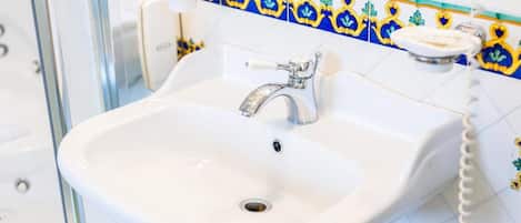 Un lavamanos de baño con una pileta de porcelana blanca, una grifería cromada y un teléfono montado en la pared.