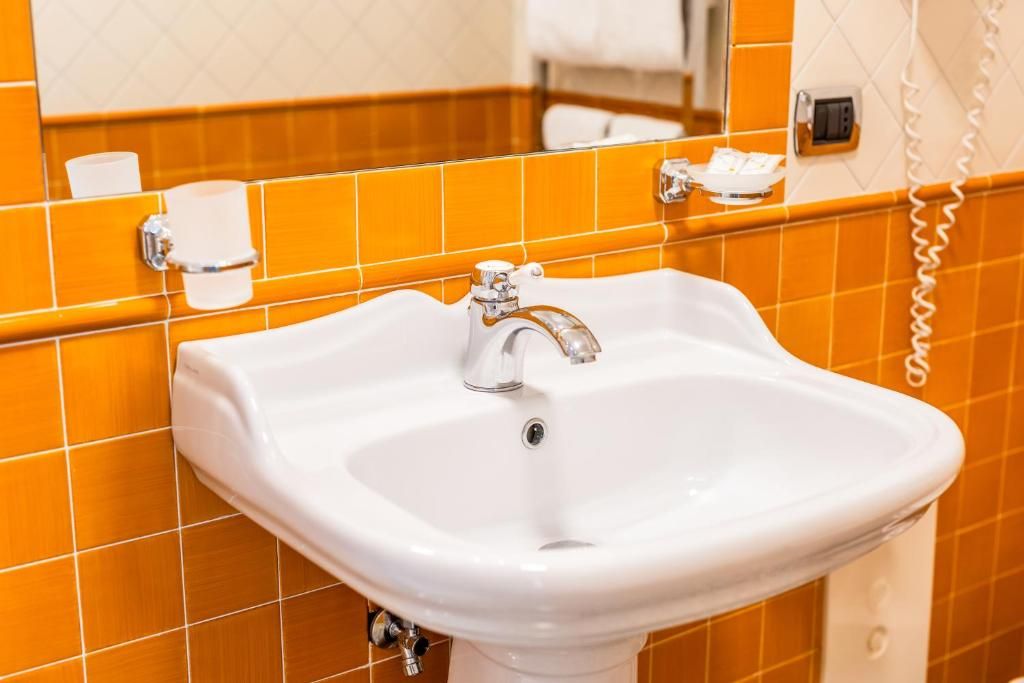 Une salle de bain avec un lavabo blanc, des murs recouverts de carreaux orange, un miroir et un téléphone.