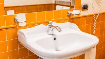 Une salle de bain avec un lavabo blanc, des murs recouverts de carreaux orange, un miroir et un téléphone.