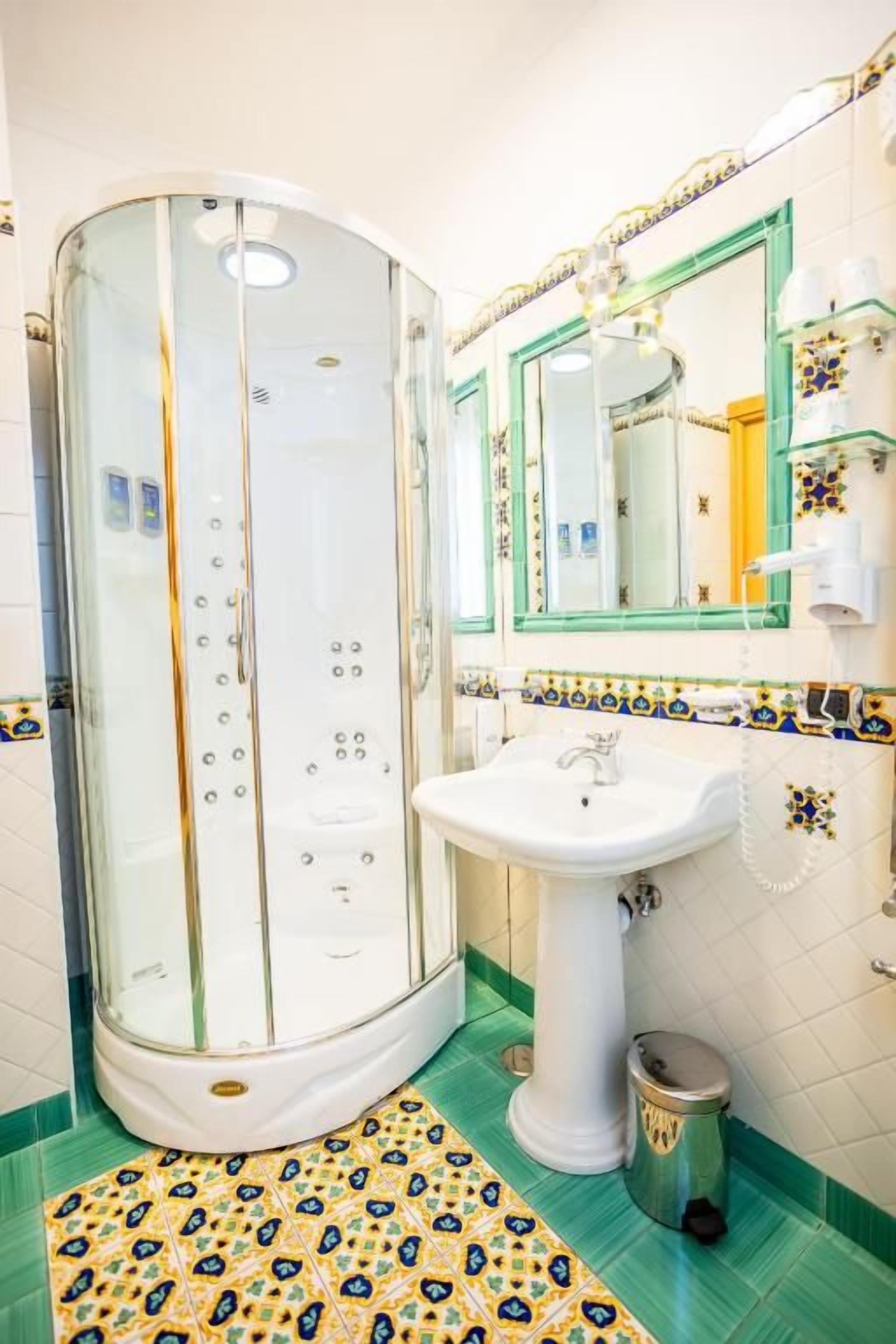 A bathroom with a glass-enclosed shower, a pedestal sink, and a tiled floor.