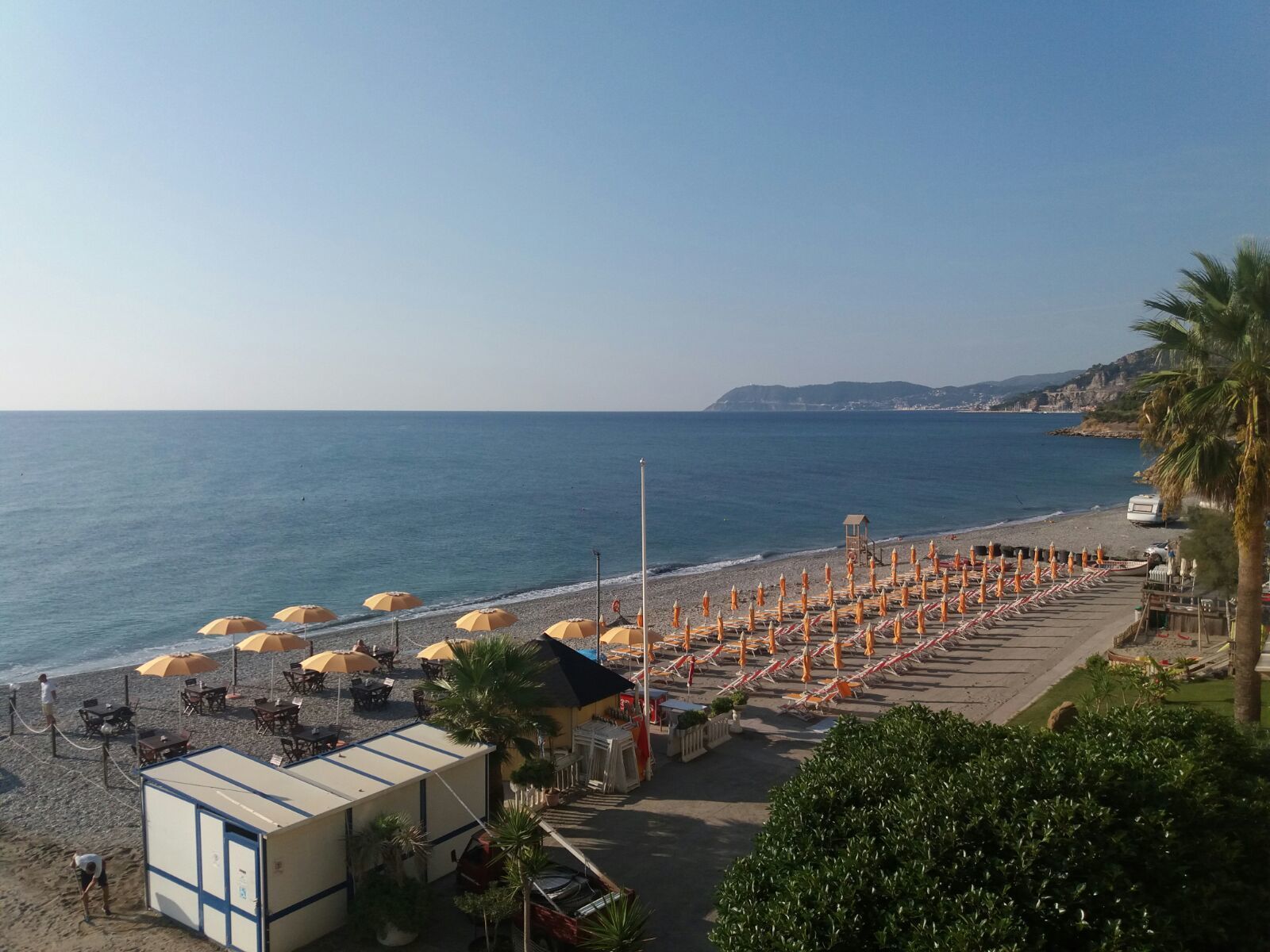 Un hotel frente a la playa con asientos exteriores y sombrillas, una torre de salvavidas y vistas al mar.