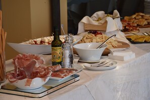 A buffet table with various food items including bowls of meat, cheese, and bread.