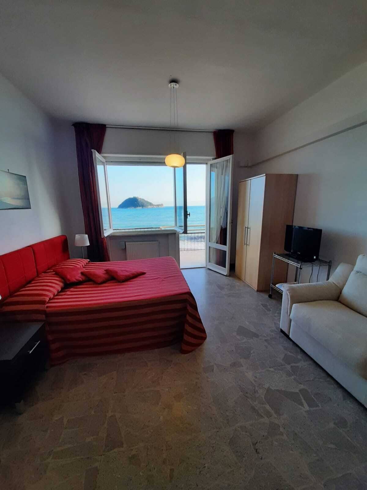 Une chambre d’hôtel avec un lit, un canapé, une télévision et vue sur la mer.