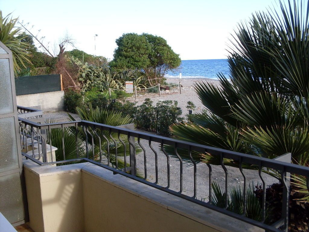 A balcony with a view of a beach, palm trees, and a fence.