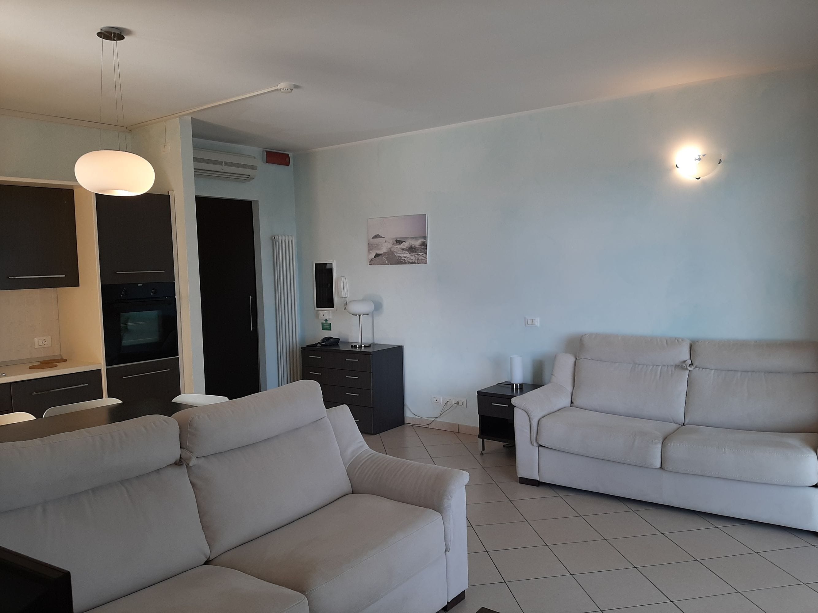 A modern living room with two sofas, a dining area with a table and chairs, and a kitchen with an oven.