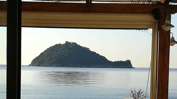 An outdoor seating area with a table and chairs facing a calm sea and a distant island. - Residence Sole (Albenga)