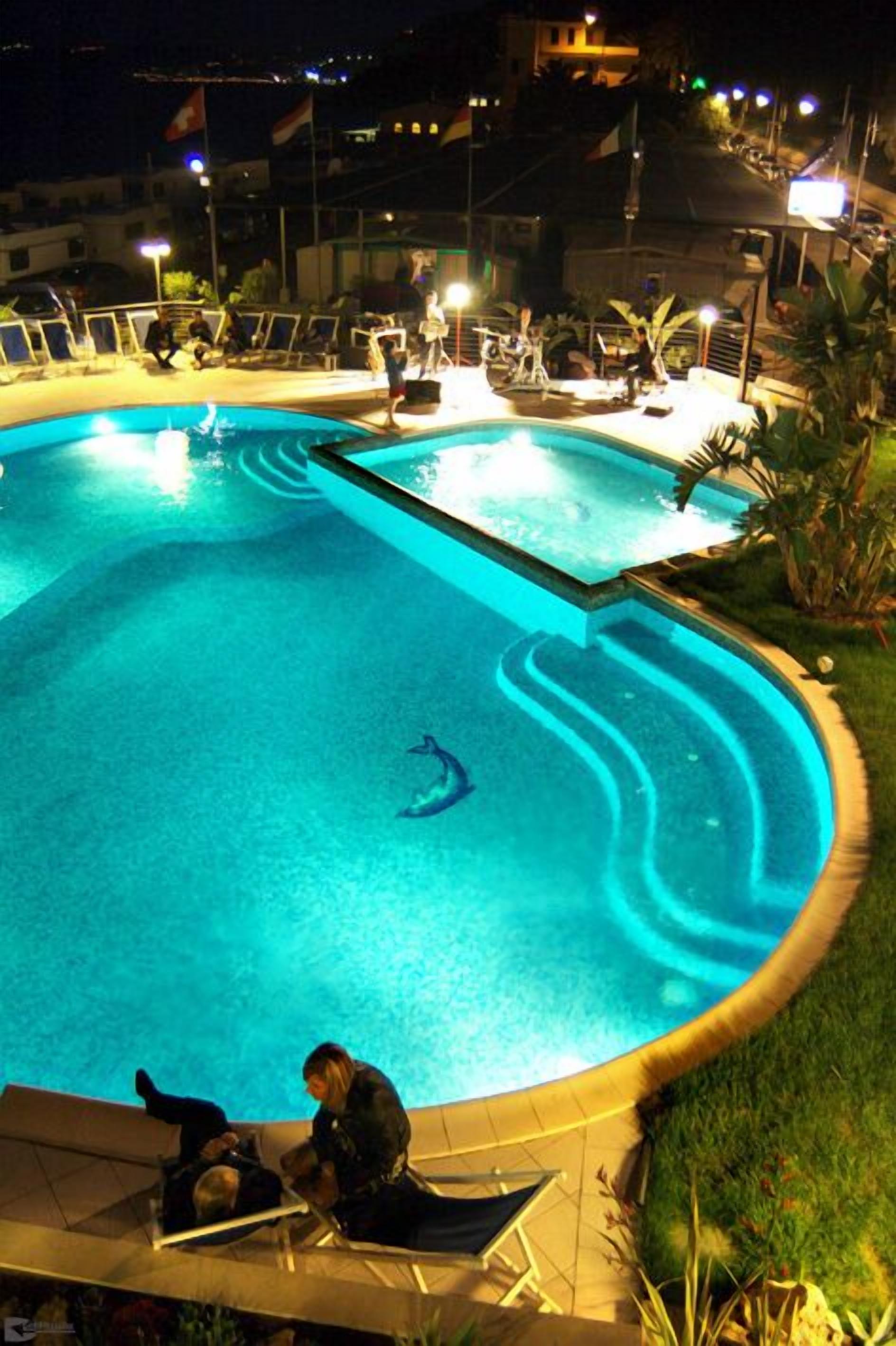 A swimming pool with a dolphin sculpture, surrounded by lounge chairs and a deck area.