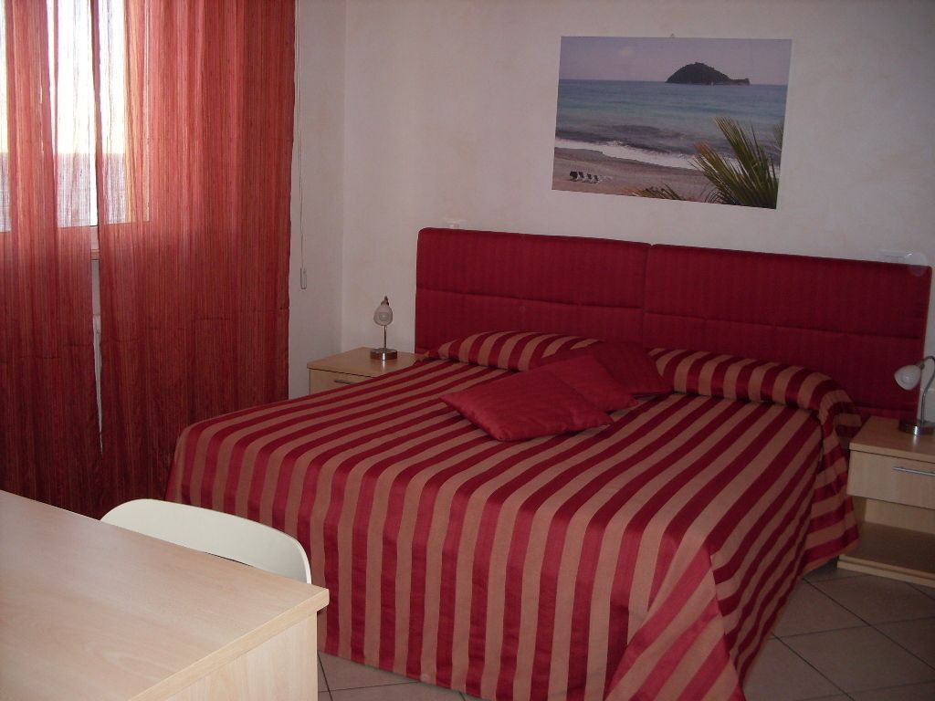 A bedroom with a bed, a nightstand, a desk, and a wall-mounted picture of a beach scene.