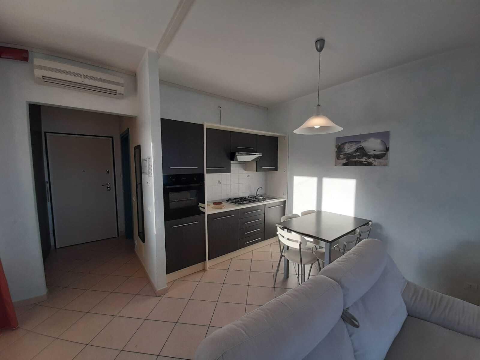 Une cuisine moderne avec des meubles de couleur sombre, un plan de travail blanc et un coin repas comprenant un canapé et une table, tous deux blancs.