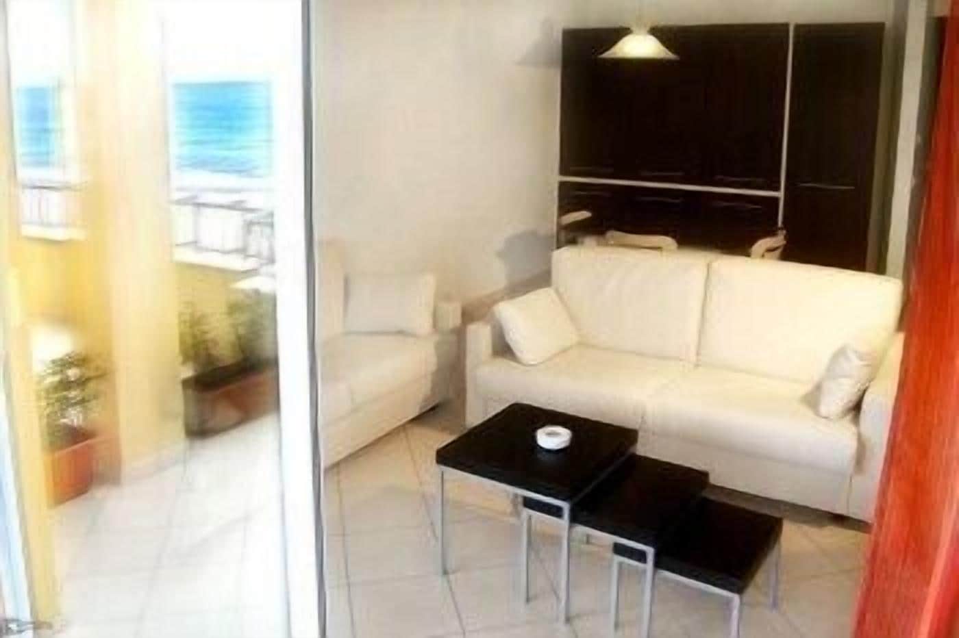 Una sala de estar moderna con un sofá blanco, una mesa de centro negra y vista al océano a través de un ventanal.