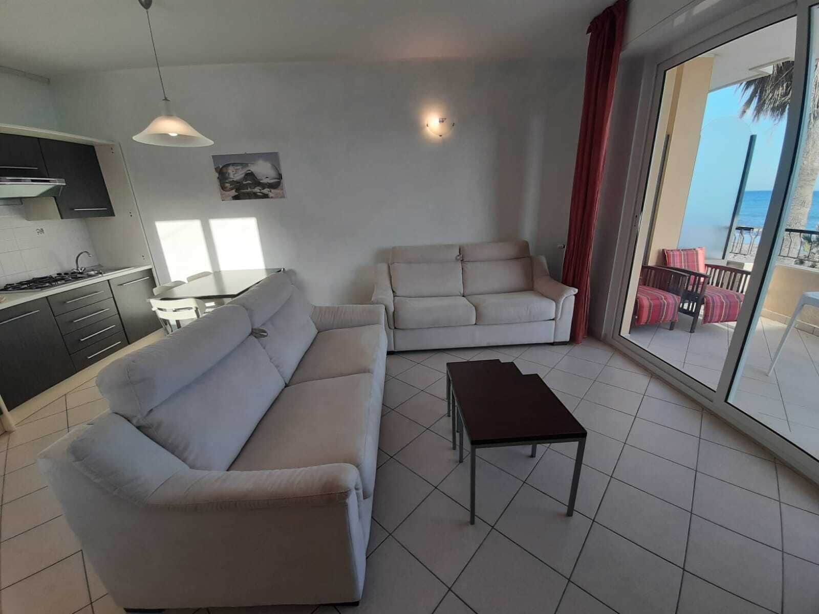 Ein modernes Wohnzimmer mit einer Couch, einem kleinen Tisch und Meerblick durch große Fenster.