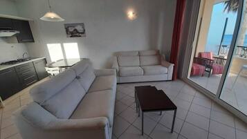 Ein modernes Wohnzimmer mit einer Couch, einem kleinen Tisch und Meerblick durch große Fenster.