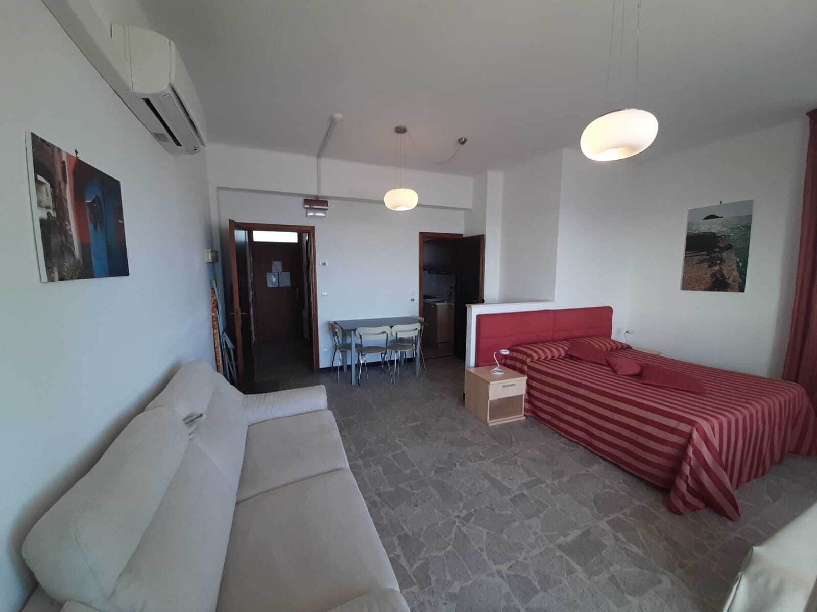 Habitació d'hotel amb un llit, un sofà, escriptori i cadires, i una cuineta.