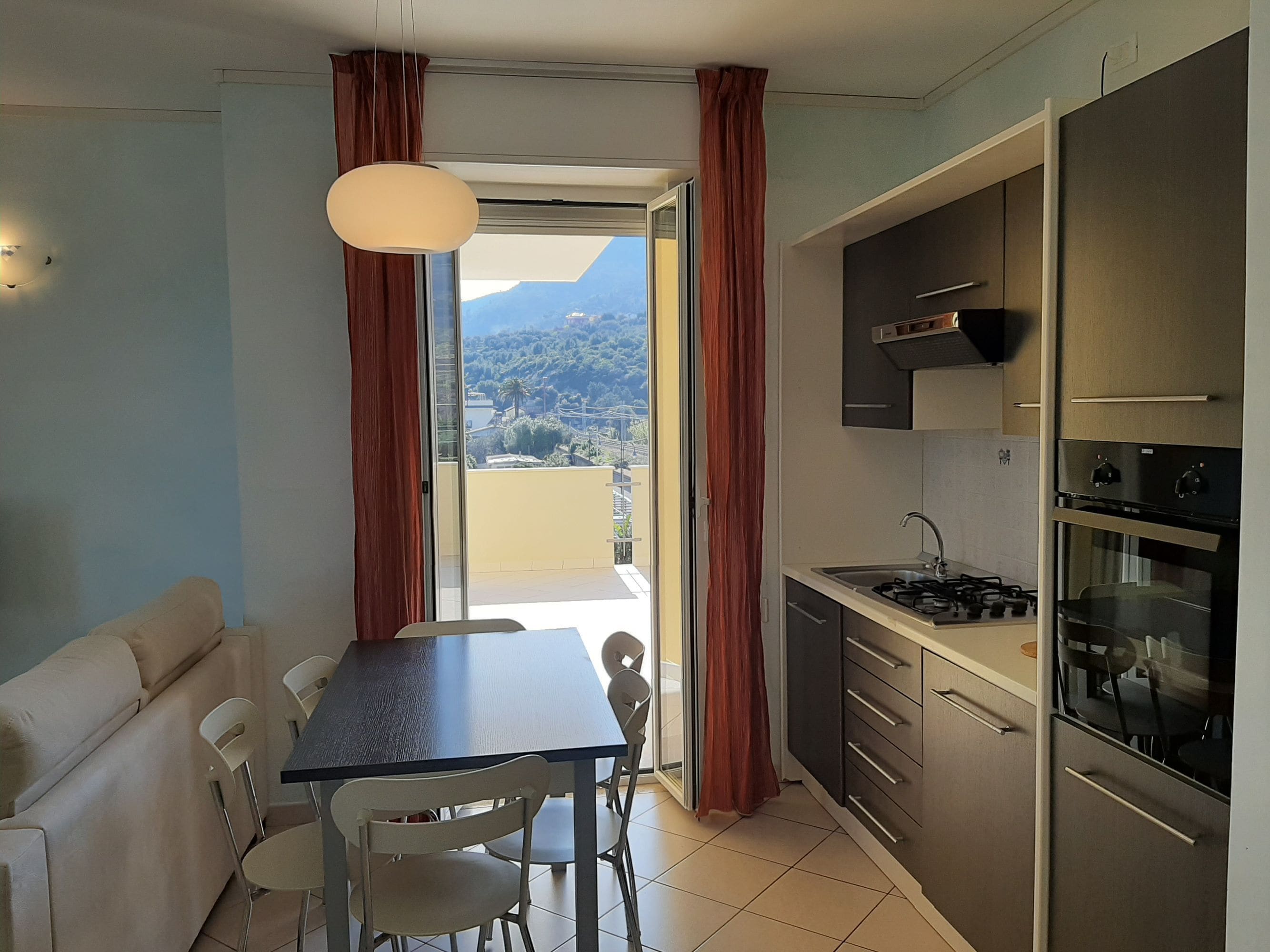 Una cocina compacta con comedor, un sofá y vista a un paisaje montañoso a través de un ventanal corredera.