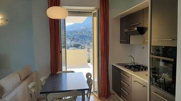 Una cocina compacta con comedor, un sofá y vista a un paisaje montañoso a través de un ventanal corredera.