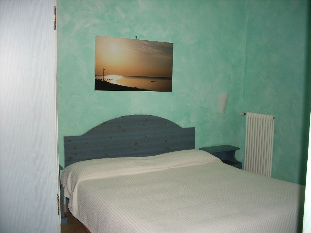 Un dormitorio con cama, mesita de noche, cuadro en la pared y radiador.