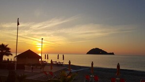 A beachside view with a sunset, a small island in the distance, and beach chairs and umbrellas. - Residence Sole (Albenga)