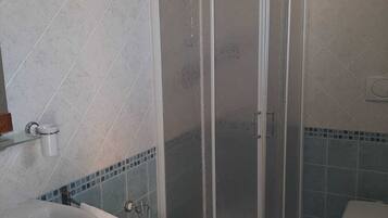 A bathroom with a shower enclosure, a toilet, and a sink.