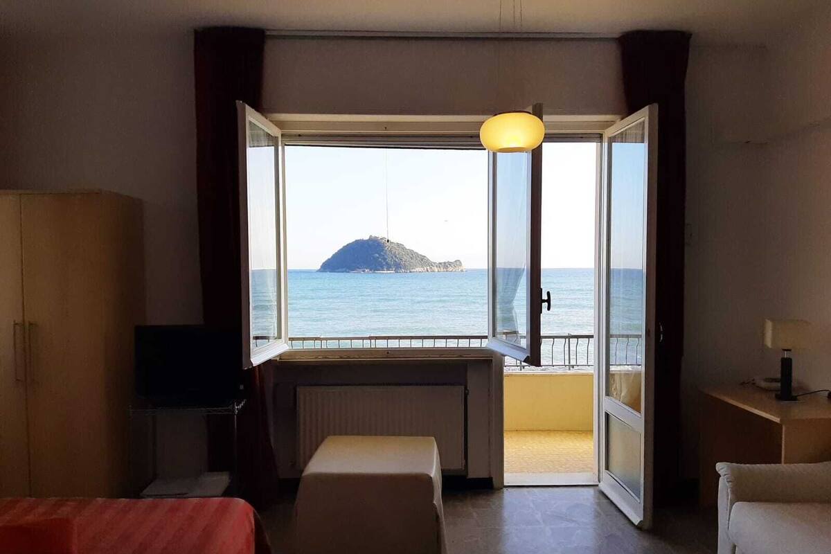 A hotel room with a large window offering a view of the sea and a small island.