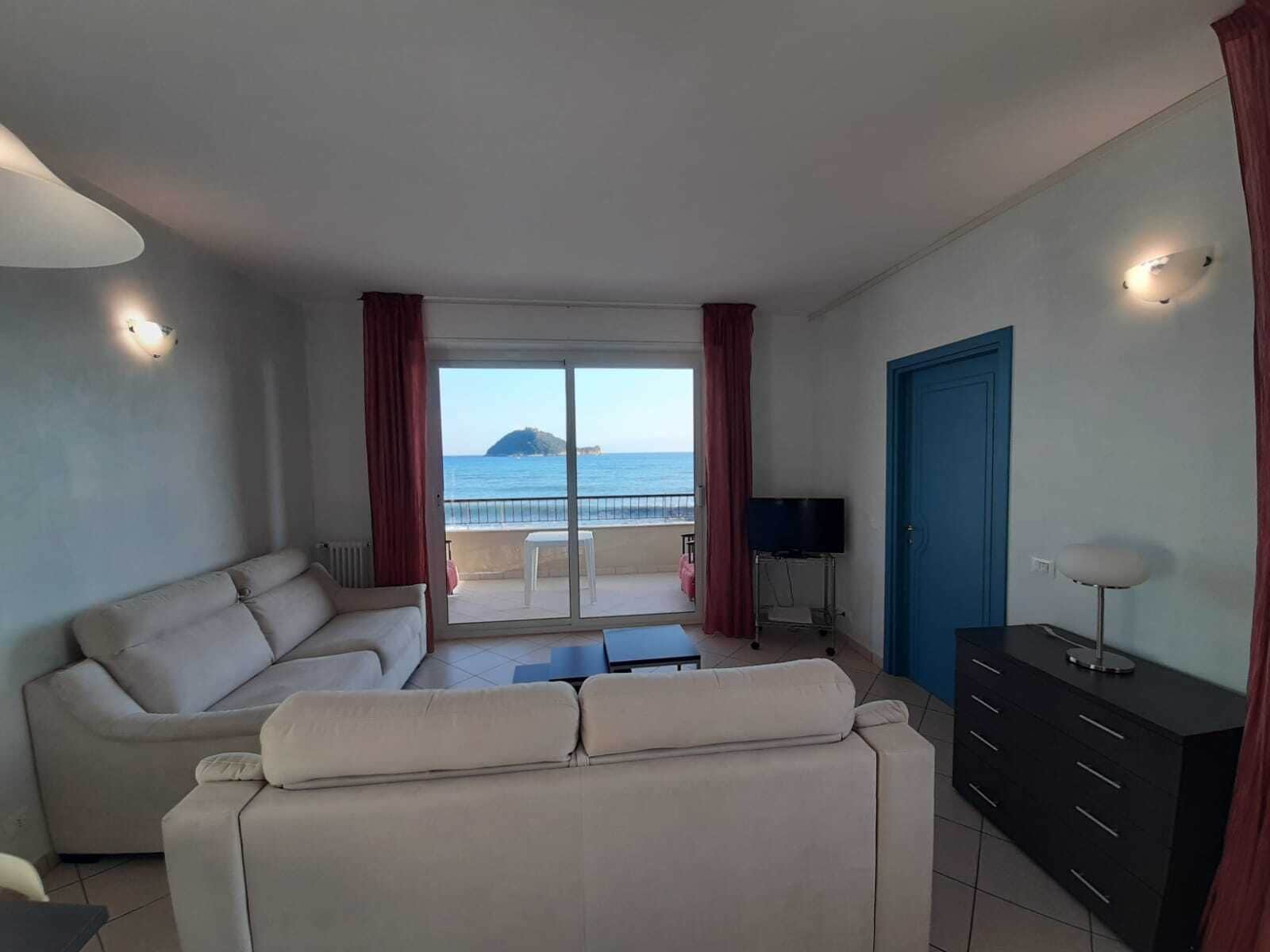 A living room with a sofa, a TV, and a view of the sea.