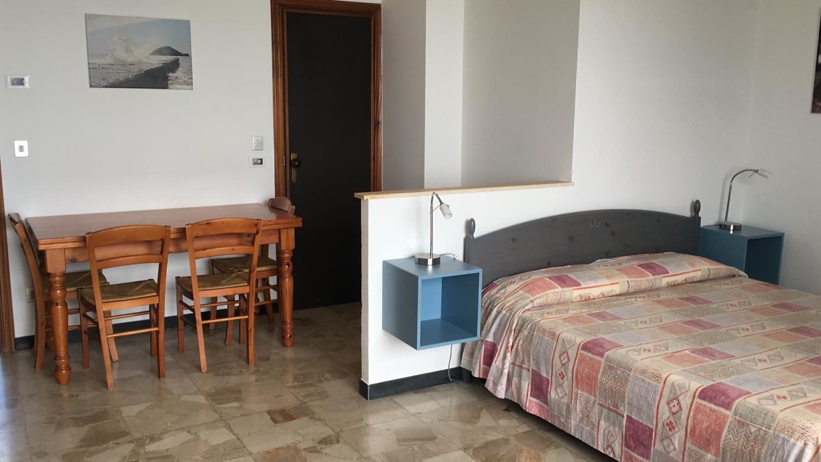 A bedroom with a bed, a bedside table, a chair, a desk, and a door.