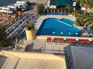 A pool area with multiple lounge chairs and umbrellas, a large pool, and RVs parked nearby.