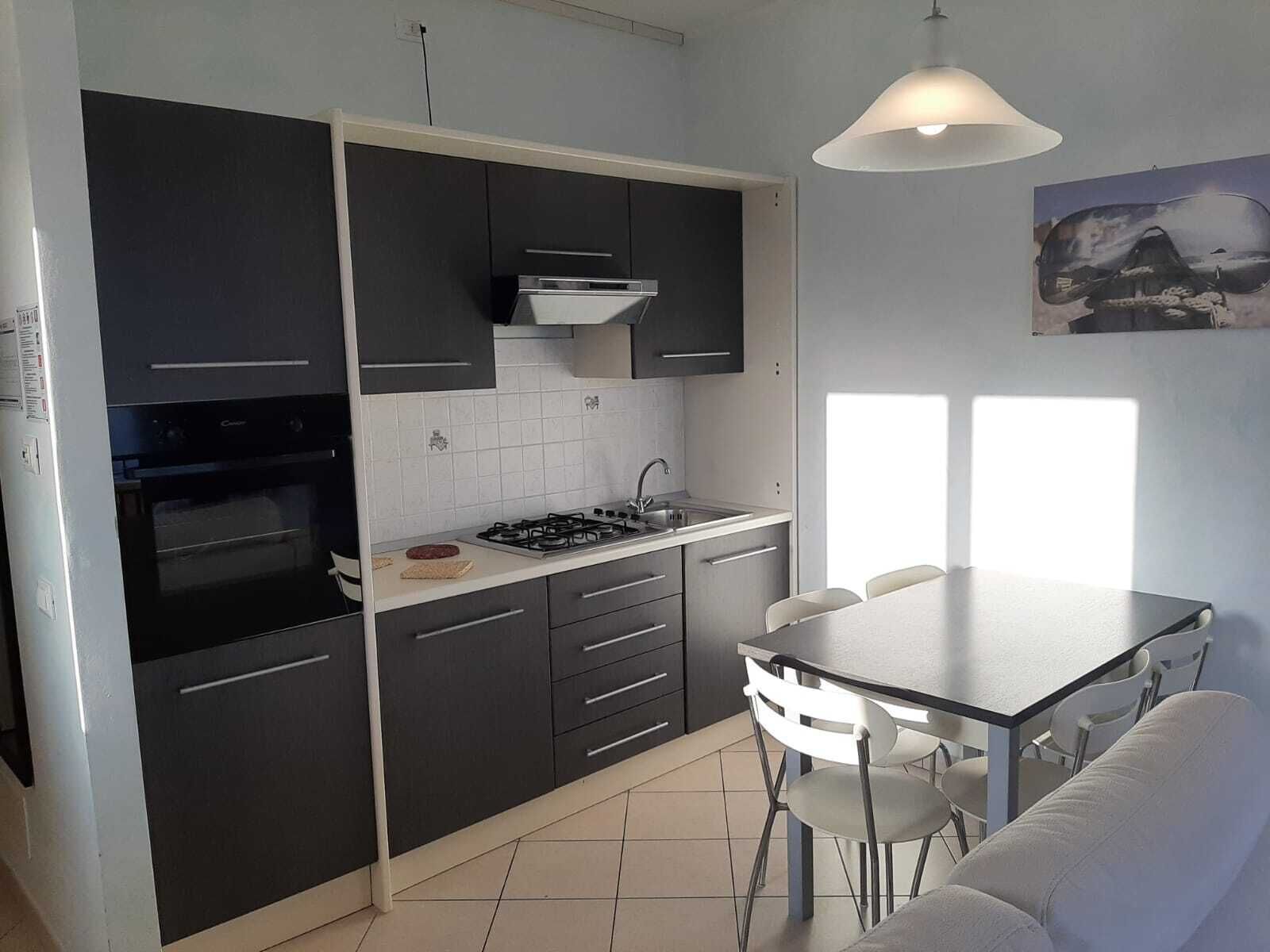 Une cuisine compacte avec des meubles de rangement sombres, une cuisinière à gaz et un petit coin repas comprenant une table et des chaises.