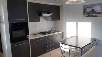 Une cuisine compacte avec des meubles de rangement sombres, une cuisinière à gaz et un petit coin repas comprenant une table et des chaises.