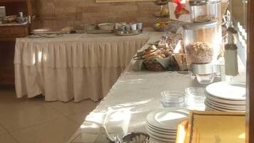 Un buffet disposé sur une longue table, avec des récipients contenant de la nourriture et un tableau accroché au mur.