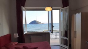 A bedroom with a bed, a desk, and a view of the sea and a small island. - Residence Sole (Albenga)