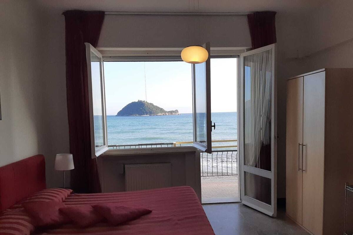 A bedroom with a bed, a desk, and a view of the sea and a small island.