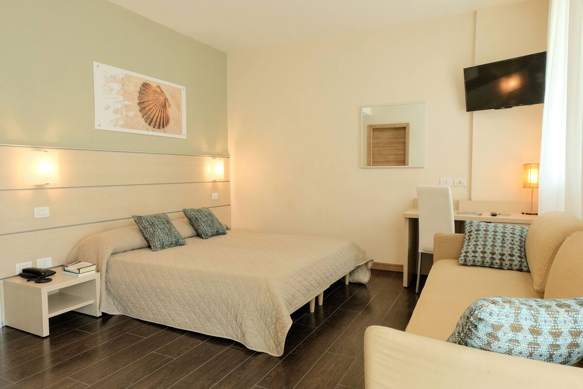 Ein Hotelzimmer mit Bett, Schreibtisch, Stuhl, Fernseher und einem Wandbild.