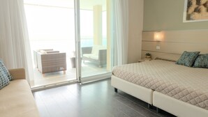 A modern bedroom with a large bed, a sofa, and a sliding glass door leading to a balcony. - Hotel Orizzonte (Jesolo)