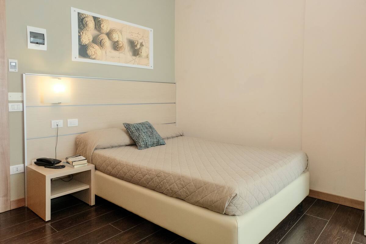 Ein ordentlich eingerichtetes Schlafzimmer mit einem Bett, Nachttisch und einem an der Wand befestigten Kunstwerk.