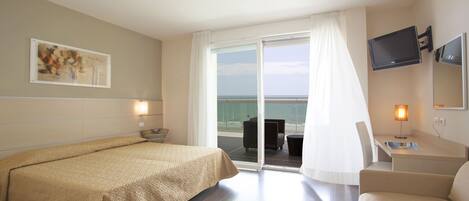 Ein Hotelzimmer mit einem Bett, einem Schreibtisch mit Stuhl, einem Fernseher und einem großen Fenster mit Meerblick.