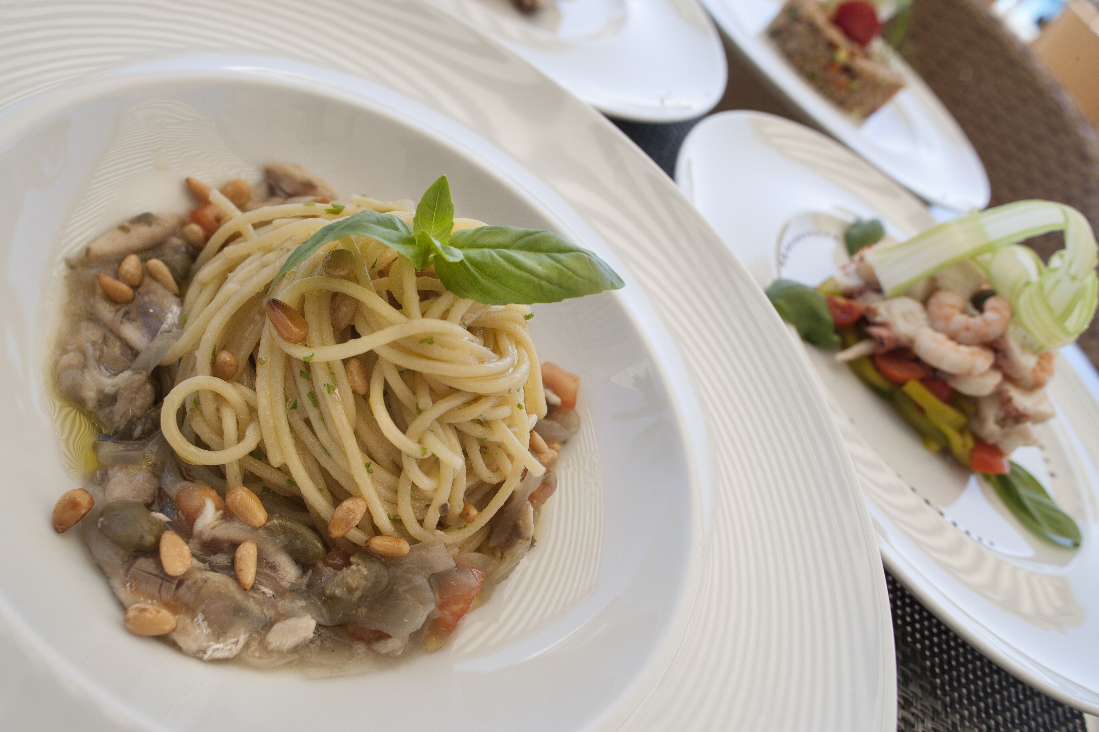 A plate of spaghetti with pine nuts and basil, and another plate with shrimp and vegetables.