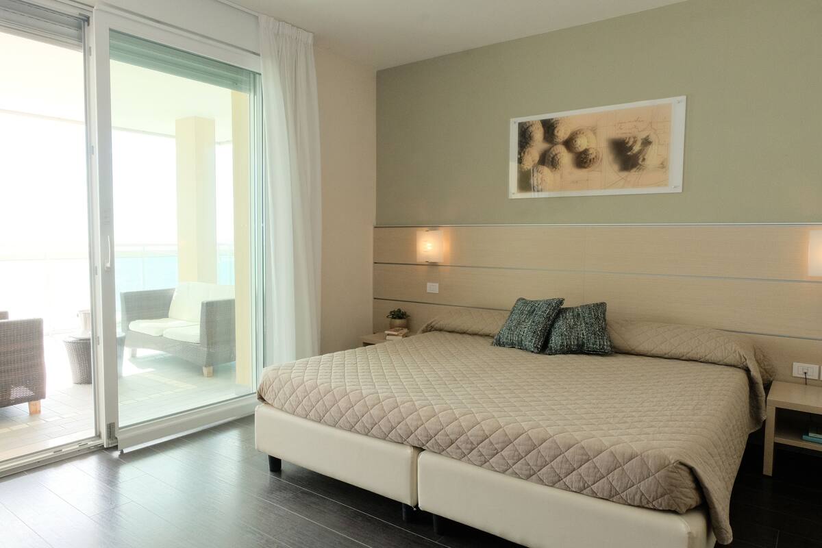Ein Schlafzimmer mit einem großen Bett, einer Schiebetür zum Balkon und einem an der Wand befestigten Kunstwerk.