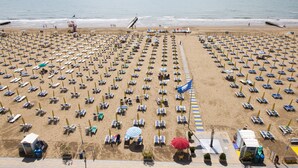 A beach with rows of sun loungers and umbrellas, a lifeguard tower, and a pier extending into the water. - Hotel Orizzonte (Jesolo)